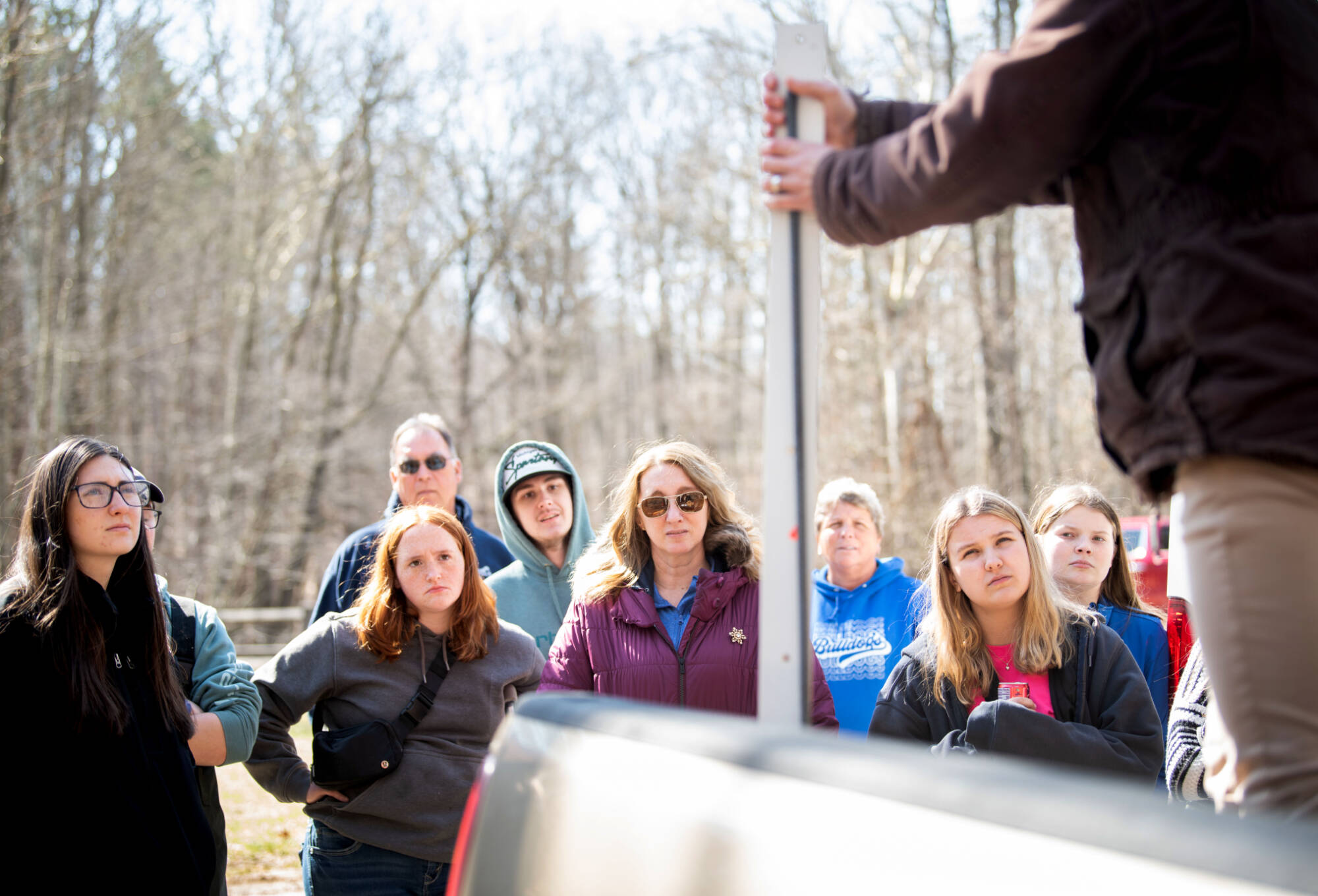 Person standing in front of group holding a measuring stick while the group listens to the person speak